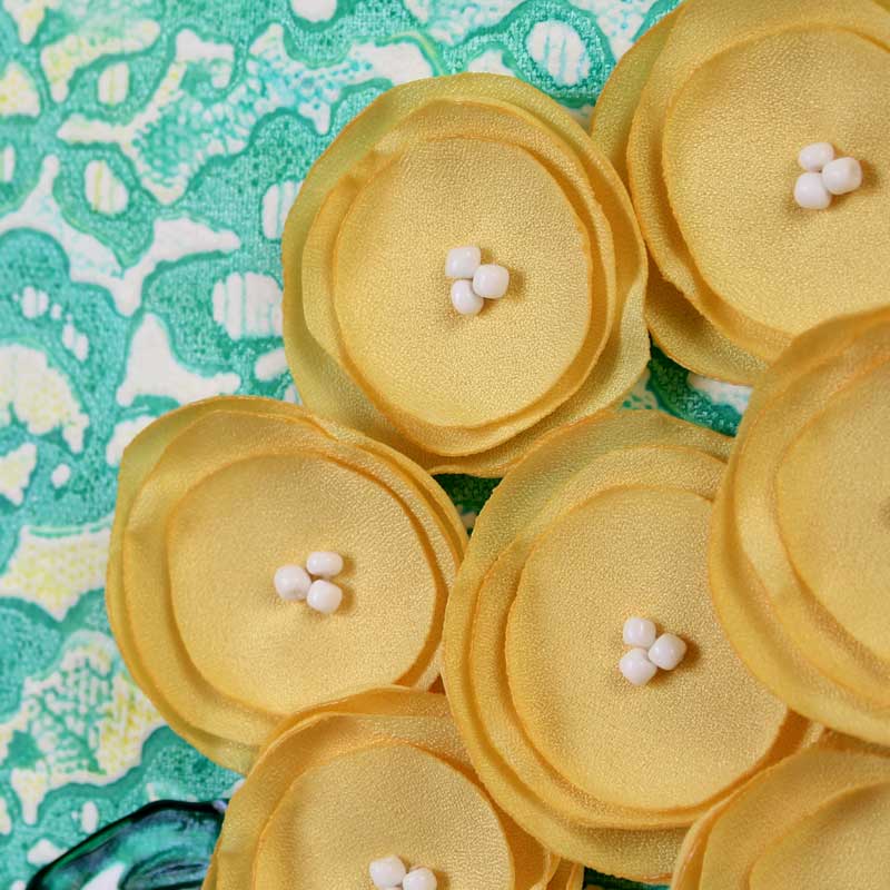 Close up of fabric flowers on yellow and teal floral still life